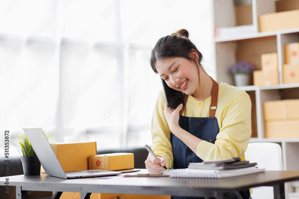 Startup SME small business entrepreneur of freelance Asian woman wearing apron using laptop and box to receive and review orders online to prepare to pack sell to customers, online sme business ideas. Startup SME small business entrepreneur of freelance Asian woman wearing apron using laptop and box to receive and review orders online to prepare to pack sell to customers, online sme business ideas.