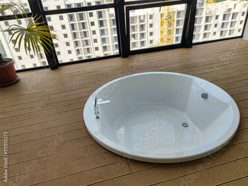 jacuzzi bathtub with wooden floor next to a large window overlooking the city