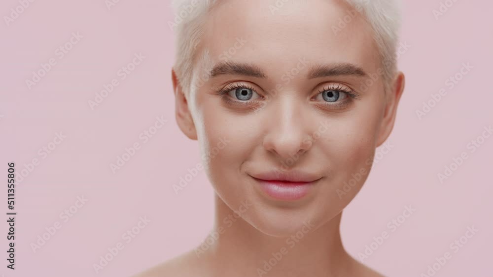 Beautiful young slim Caucasian woman with short fair hair moves her hands away from her face and looks at the camera smiling for it on pale pink background | Face skin protection concept Beautiful young slim Caucasian woman with short fair hair moves her hands away from her face and looks at the camera smiling for it on pale pink background | Face skin protection concept