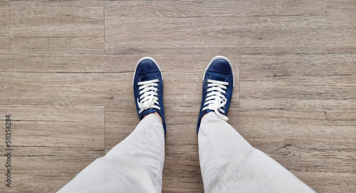 feet in denim sneakers standing on wooden vinyl floor, selective focus. fashion hipster cool man with wblue sneakers and beige pants, soft vintage toned colors for beginning concept. photo