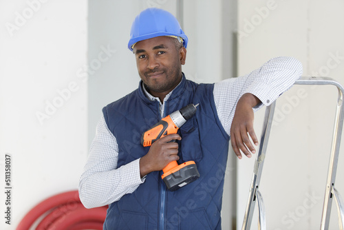 Photography happy male builder standing on ladder with drill