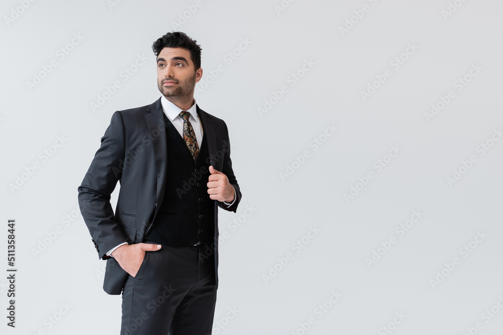 muslim groom in formal wear standing with hand in pocket isolated on grey. muslim groom in formal wear standing with hand in pocket isolated on grey.