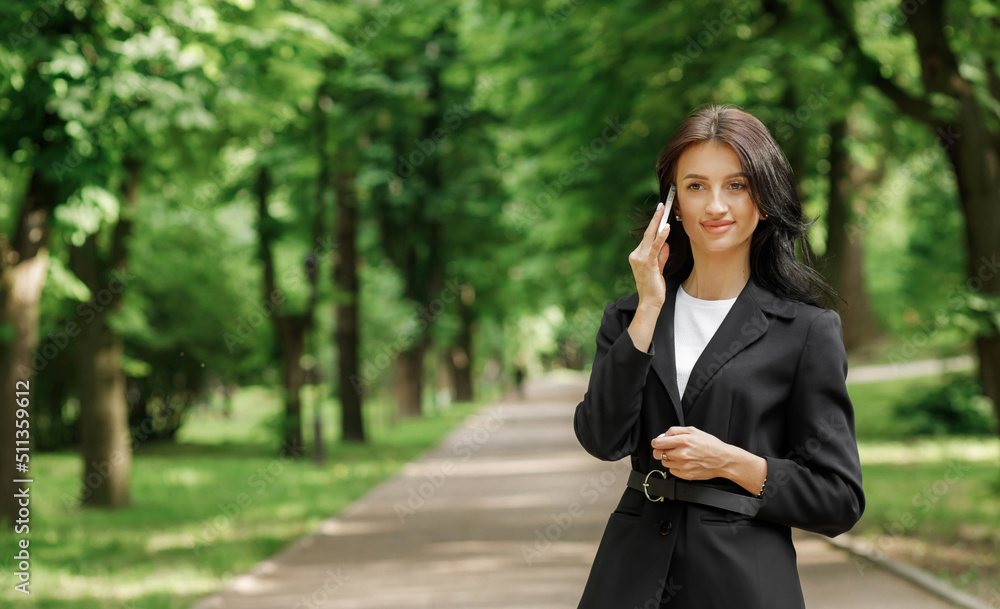 Business woman use cellphone outdoors. Beautiful focused young girl wearing a formal suit in the park.