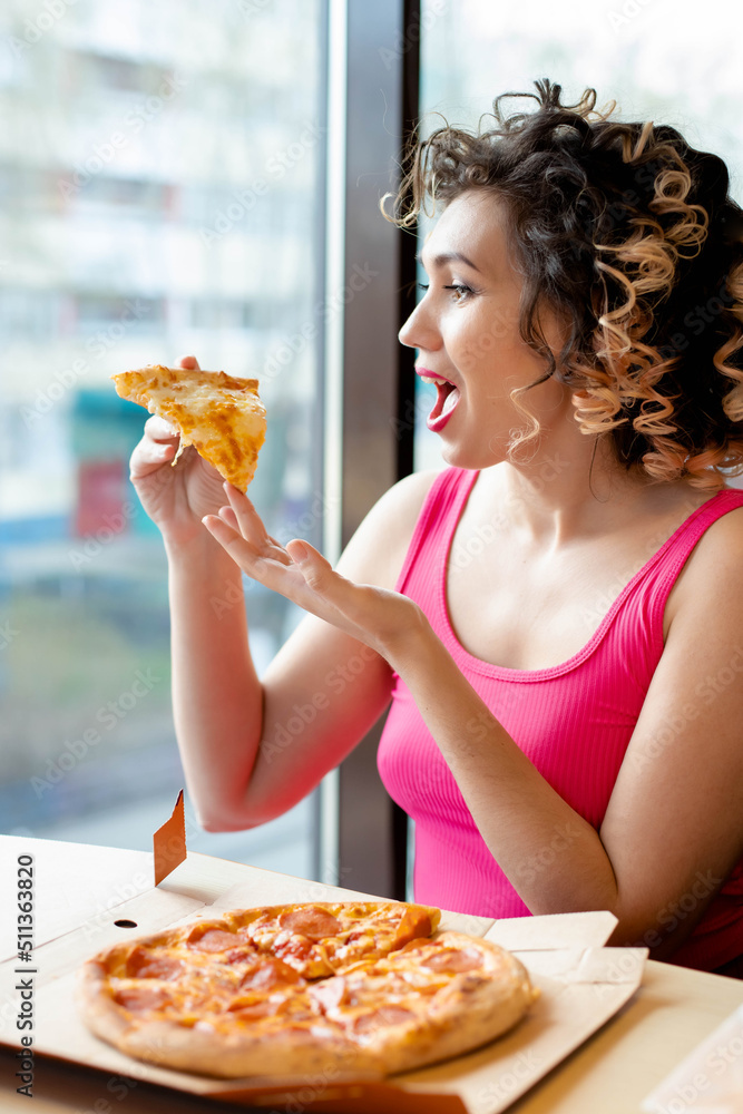 a young woman is wearing pink T-shirt eating pizza in a cafe