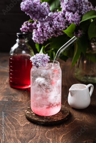 Refreshing cold lilac lemonade in the making. Sparkling soda water  lilac syrup  flowers  highball glass filled with ice cubes.