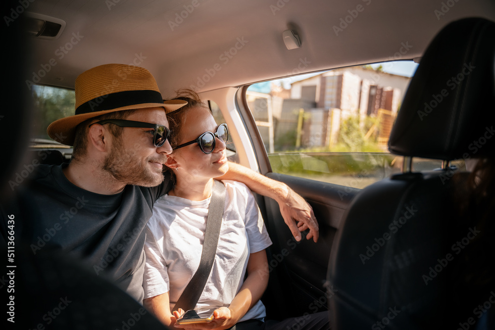 Young cheerful happy couple of travelers sitting in the car in the back seat looking out the window