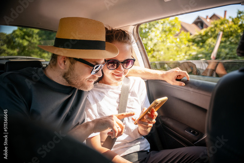 Obraz na płótnie Young cheerful happy couple of travelers sitting in car looking at smartphone screen, travel comfort safety taxi w salonie