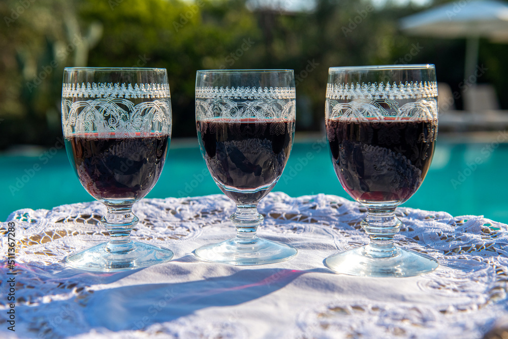3 bardzo ładnie zdobione kieliszki z czerwonym winem stojące na tacy na tle basenu - obrazy, fototapety, plakaty 