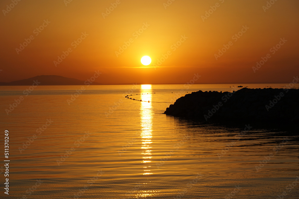 Scenic golden hour at seascape during vibrant orange color tone sunset with contrasting black silhouette