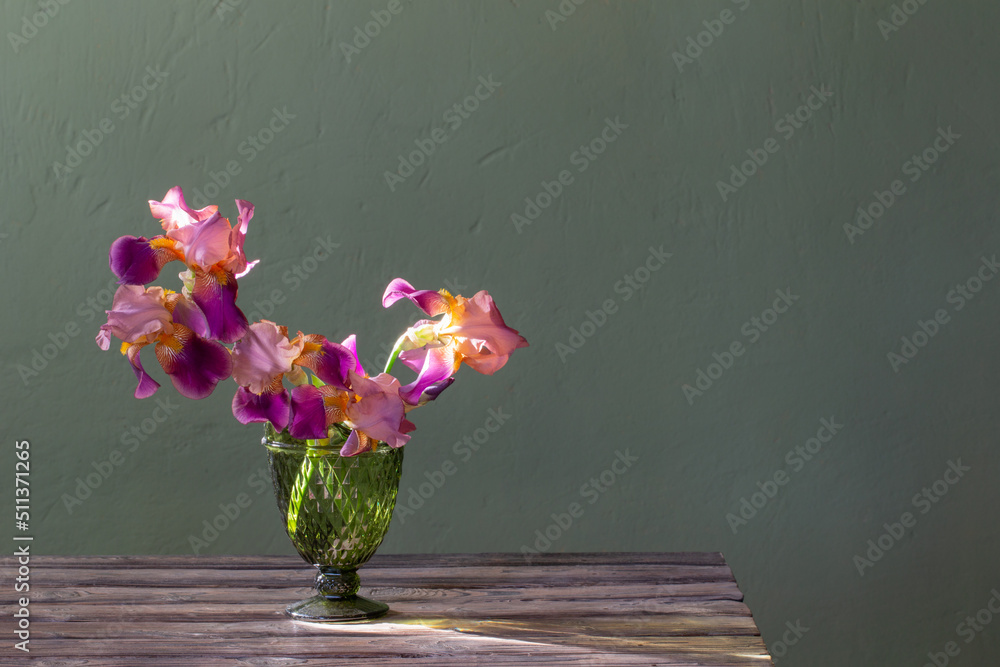 irises in  beautiful glass vase against  green wall