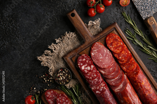 Sausage and cold cuts. Types of different loaf sausages on an old wooden board on black background and burlap with cherry tomatoes, rosemary, garlic and spices.Rustic.Top. Background image, copy space