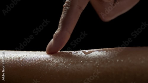 Macro shot of young African American woman strokes her good-looking wet skin on black background | Skin texture shot for skin hydration concept