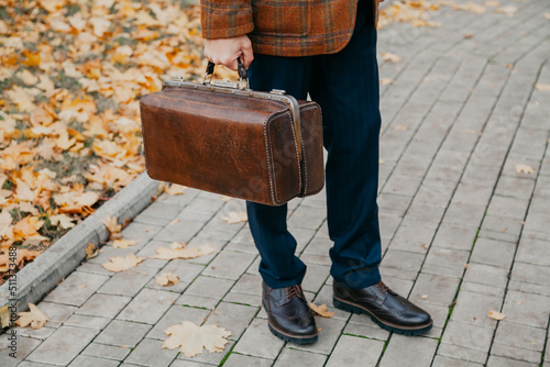 Man with carpetbag in jacket stands in alley of autumn park photo