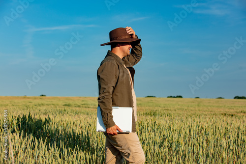 Farmer in hat with laptop computer on wheat field