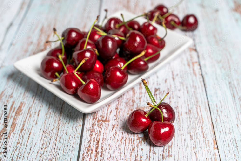 white plate with red cherries on wooden table. Seasonal fruit concept white plate with red cherries on wooden table. Seasonal fruit concept