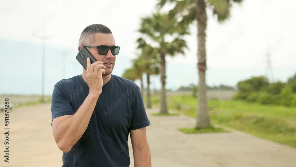 A man on the phone walks along the promenade with palm trees. Call from vacation on a background of palm trees slow motion A man on the phone walks along the promenade with palm trees. Call from vacation on a background of palm trees slow motion