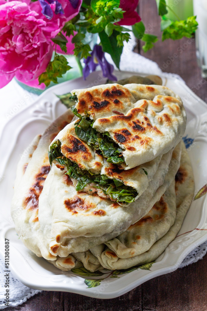 Traditional Armenian flatbread with greens zhengyalov hats, served with yogurt on the background of a bouquet.