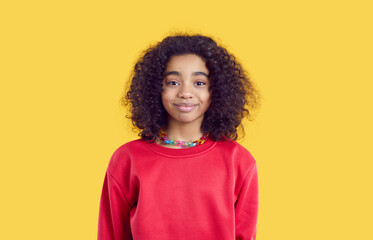 Happy child in casual clothes. Positive little kid isolated on solid bright yellow color background. Studio head shot of pretty African American girl in red sweatshirt looking at camera and smiling