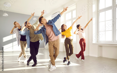 Happy energetic young hip-hop dancers dance together in bright spacious dance studio. Active young women and men in modern casual clothes pursue their hobbies and learn new dance movements together. photo