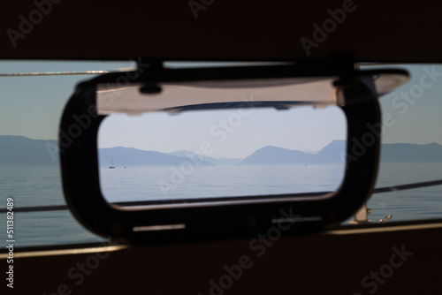view from inside a sailboat out of a window to the sea with another sailboat and islands