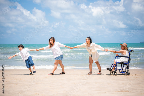disabled woman in a wheelchair with family and shaking hands together on the beach(vintage tone)