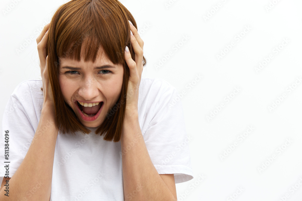 a close horizontal studio photo of a red-haired woman screaming loudly clutching her head from shock. a close horizontal studio photo of a red-haired woman screaming loudly clutching her head from shock.