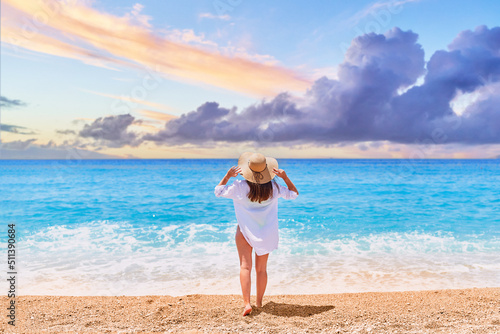 Back of one alone inspired happy beautiful brunette woman in straw hat and white shirt standing on sea beach in summer sunny day