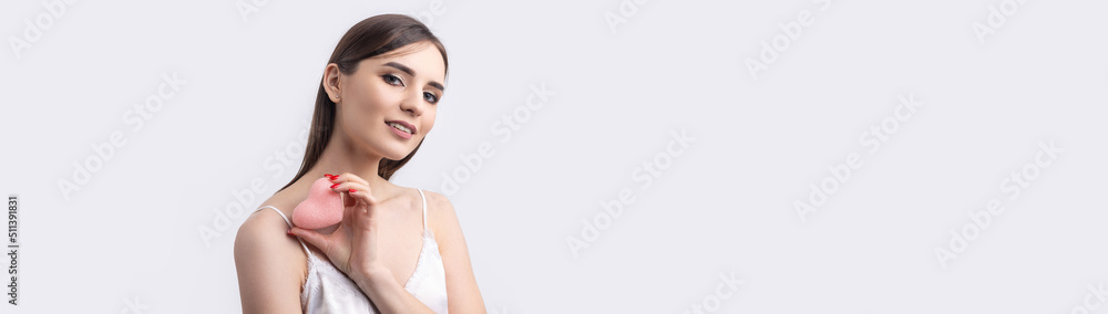 Beautiful smiling woman with clean skin, natural make-up and white teeth on a gray background. Holding a pink hygienic heart. Beautiful smiling woman with clean skin, natural make-up and white teeth on a gray background. Holding a pink hygienic heart.