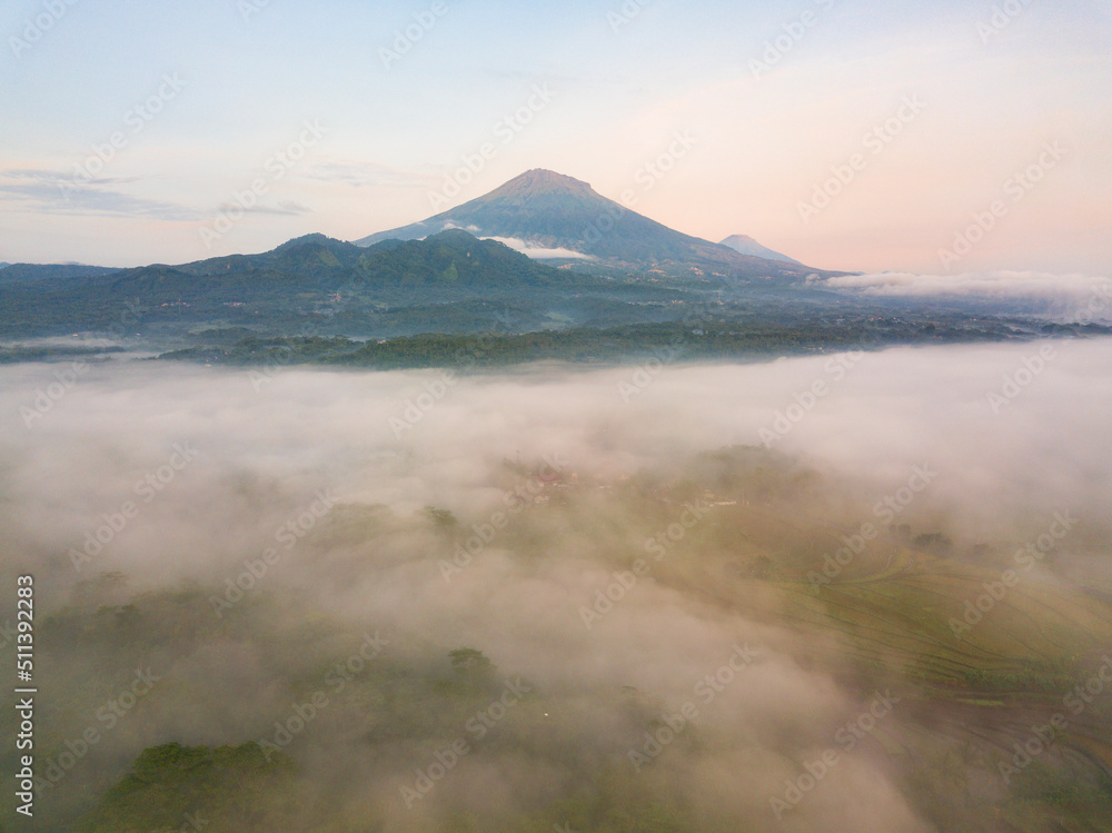 Drone photo of Mount Sumbing with sea of fog covered the land of plantation and trees in the morning. Central Java, Indonesia Drone photo of Mount Sumbing with sea of fog covered the land of plantation and trees in the morning. Central Java, Indonesia