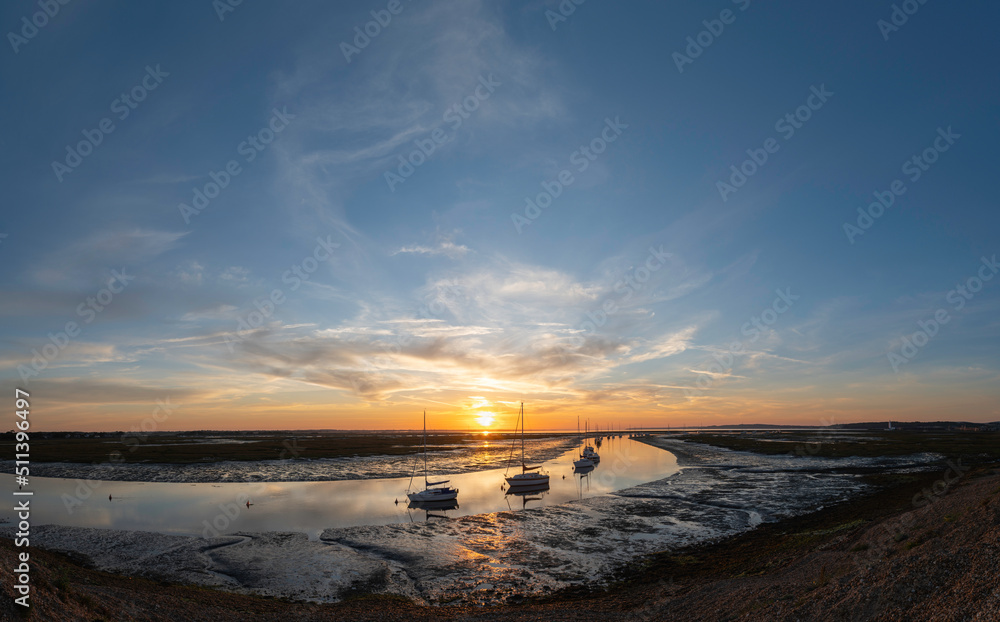 Naklejka premium Sunrise with sailing boats moored on Mount lake with Hurst lighthouse in the distance with mudflats exposed with the low tide at Hurst spit. Milford on Sea, Hampshire, UK. 
