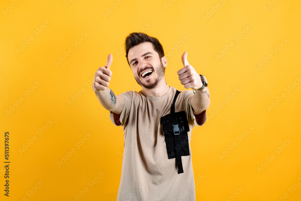 Fototapeta premium Portrait of man wearing beige tee posing isolated over yellow background doing hand gesture for great accomplishment. Show two hands thumbs up have good mood.