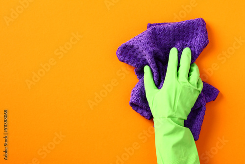 Female hand in protection glove with cleaning rag on orange background photo