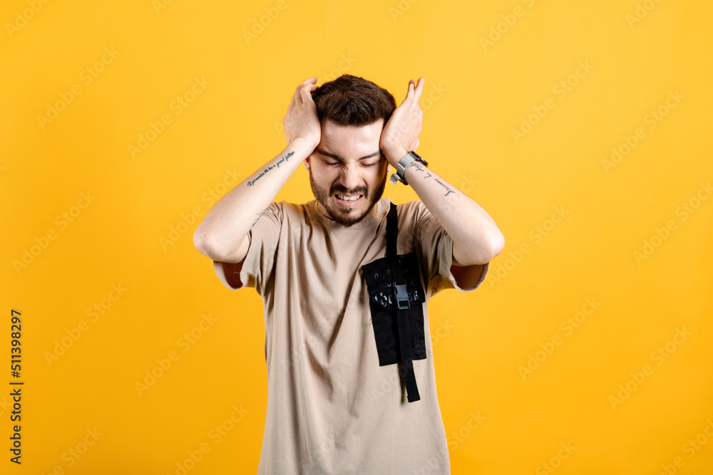 Caucasian man wearing beige tee posing isolated over yellow background hand on head for pain in head because stress. Suffering from migraine. Caucasian man wearing beige tee posing isolated over yellow background hand on head for pain in head because stress. Suffering from migraine.