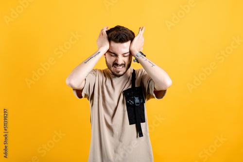 Caucasian man wearing beige tee posing isolated over yellow background hand on head for pain in head because stress. Suffering from migraine.