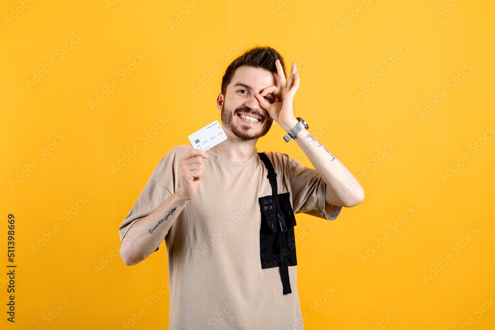 Portrait of cheerful man wearing beige t-shirt posing isolated over yellow background holding credit bank card and showing okay gesture looking at the camera. Portrait of cheerful man wearing beige t-shirt posing isolated over yellow background holding credit bank card and showing okay gesture looking at the camera.