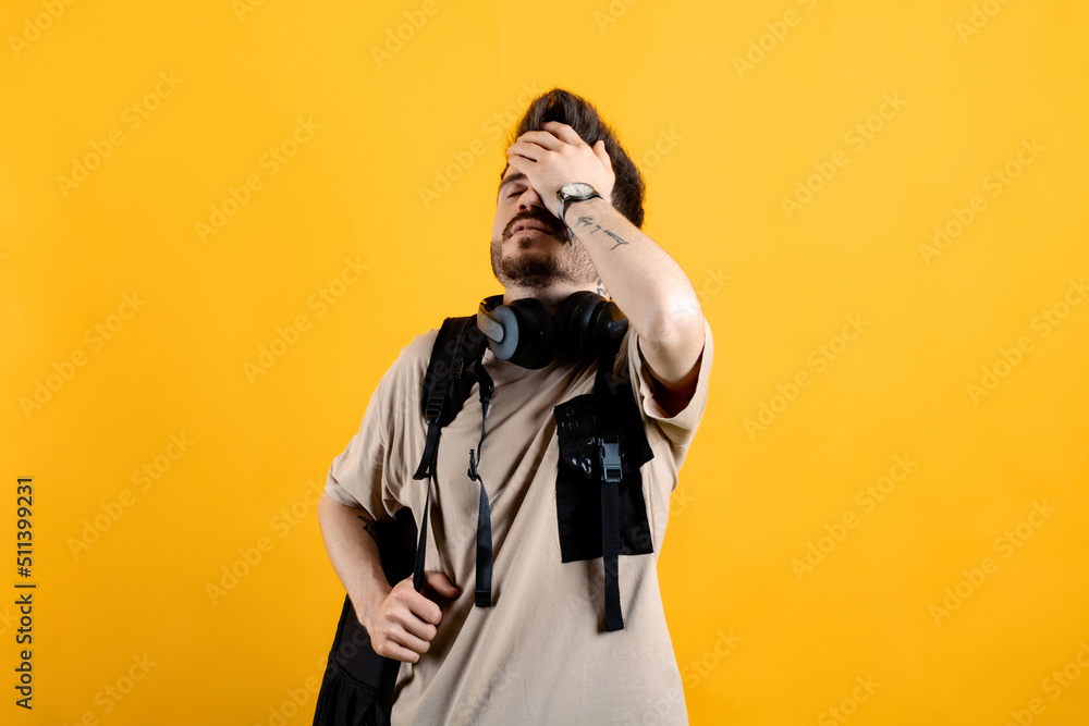 Caucasian man wearing beige tee posing isolated over yellow background suffering headache and holding hands on forehead. Education in university college, backpack concept. Caucasian man wearing beige tee posing isolated over yellow background suffering headache and holding hands on forehead. Education in university college, backpack concept.