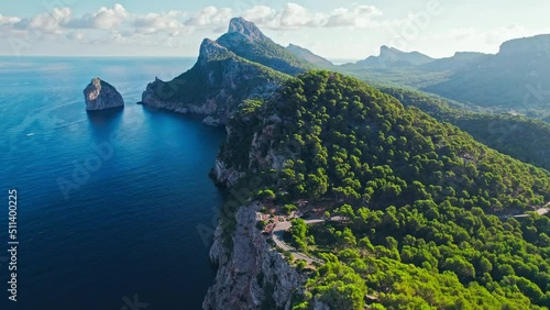 Aerial top view of a curved road by the edge of a green coast in Majorca, Spain. Scenic view of a mountainous region with a road in the middle of the forest in Mallorca, Balearic Islands.