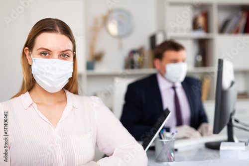 Portrait of young business woman in medical face mask looking at camera in office. Concept of precautions and social distancing in COVID 19 pandemic