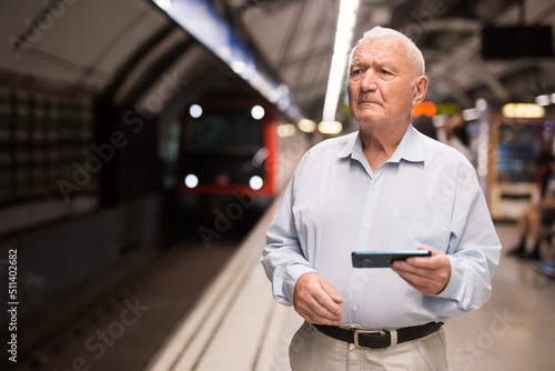 Senior man with smartphone in hands standing in metro station and using his smartphone.