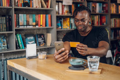 African american man using smartphone and credit card in a cafe