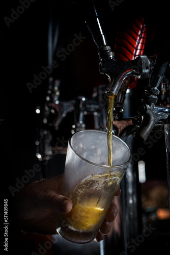 Beer pouring down from tap into cold pint glass at brewery