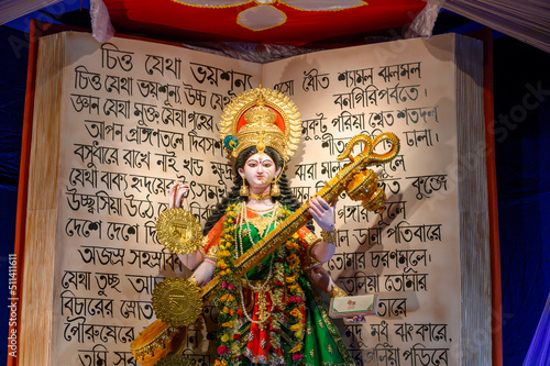 Howrah, West Bengal, India - 17th February 2021 : Idol of Goddess Saraswati being worshipped inside pandal , a temporary temple, at night. Bengali poems of R.N.Tagore are written as decoration. photo