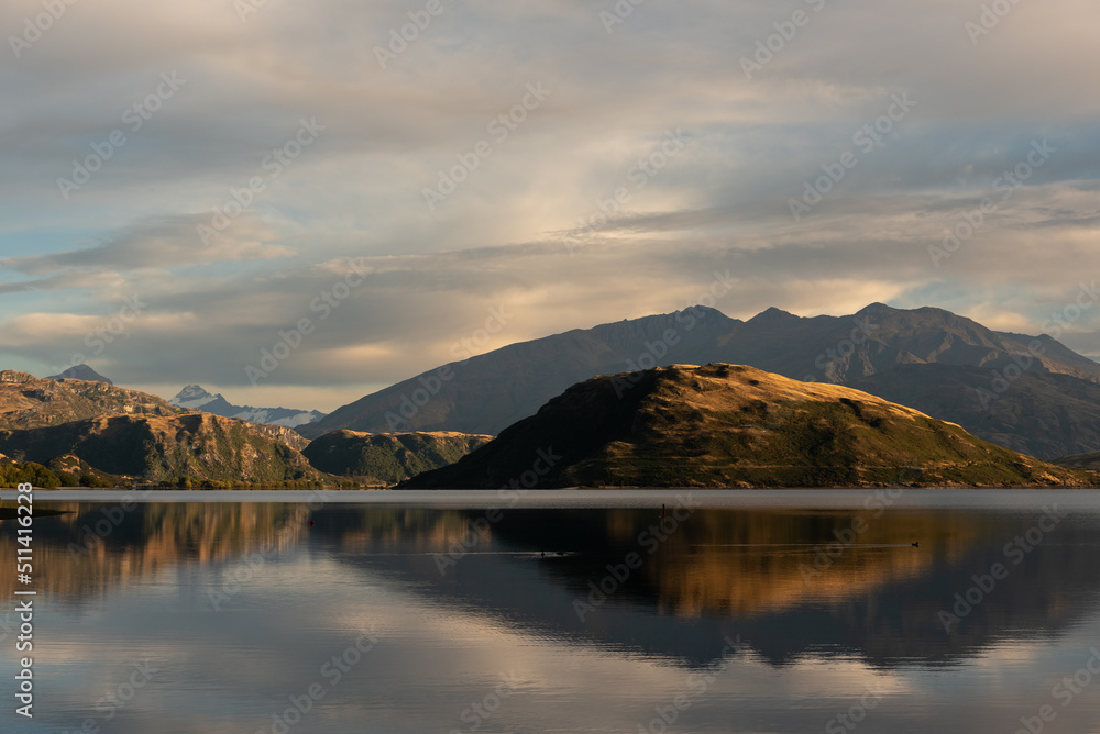 An early morning view from Glendhu Bay on Lake Wanaka with Roy's Peninsula and the mountains of Mount Aspiring National Park reflected in the calm water. Otago, South Island, New Zealand.