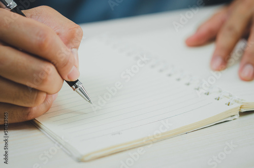person holding a pen writing notes at a notebook. © khunkornStudio