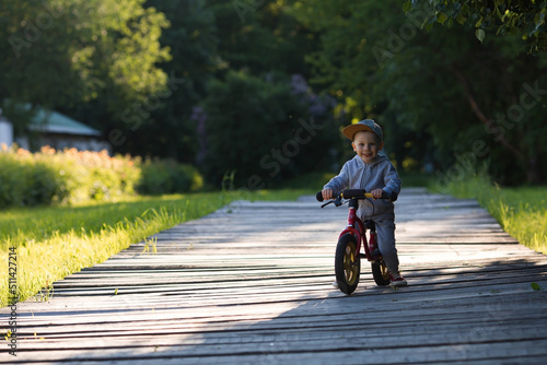 Funny little boy riding a bicycle (running bike) outdoors. A happy child walks in the spring park. The kid is dressed in a tracksuit and sneakers.