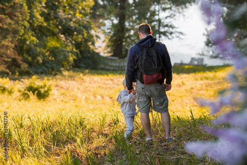 A man and a boy go hiking in the summer forest with a backpack for hiking. Portrait of a father and son sitting on his father's shoulders in the forest at sunset. The concept of travel.