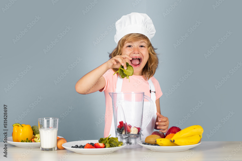 Excited funny chef cook. Child wearing cooker uniform and chef hat hold spinach preparing vegetables on kitchen, studio portrait. Cooking, culinary and kids food concept. Excited funny chef cook. Child wearing cooker uniform and chef hat hold spinach preparing vegetables on kitchen, studio portrait. Cooking, culinary and kids food concept.