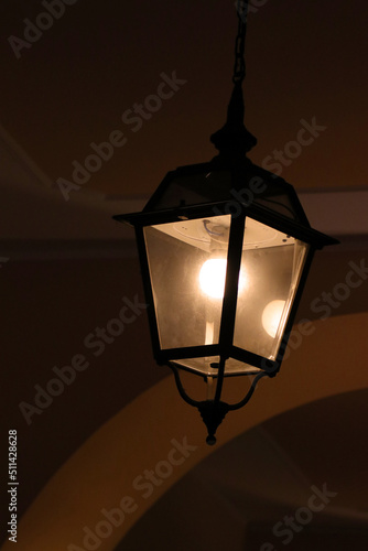 イタリア、ミラノの厳寒の門灯。Night view of an slightly lit old squared glass lamp hung on the wall of a building.