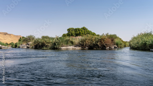 On the river bank there are thickets of green vegetation, picturesque boulders. A sand dune against a clear blue sky. Copy space. Egypt. Nile