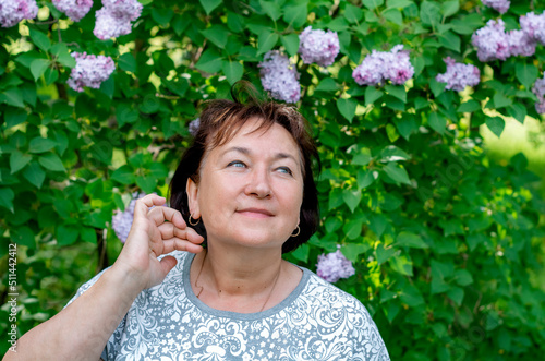 portrait of a happy attractive mature woman 50-60 years old on a blurry background of beautiful shrubs, travel and retirement, fashion and beauty